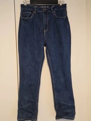 Mörkblå raka jeans med hög midja - Snygga mörkblå jeans med raka ben och hög midja. Klassisk femficksmodell med kontrastsömmar och dragkedja fram. Perfekta till en avslappnad stil och lätta att matcha med olika toppar.