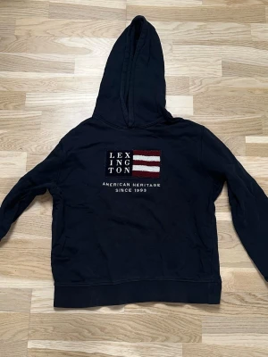 Mörkblå Lexington hoodie - En mörkblå hoodie från Lexington! Är fortfarande i ett bra skick och den är inte använd överdrivet många gånger! VIKTIGT: Storleken på den är 158/164 men har krympt en aning i tvätten så det är viktigt att tänka på.             Säljes pga att den är för liten.