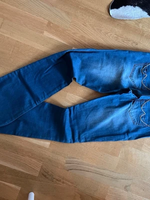 Blå bootcut jeans med råa kanter - Snygga blå bootcut jeans med slitningar och råa kanter nertill. Jeansen har framfickor och bakfickor med dekorativa sömmar. Perfekta för en avslappnad och trendig look.