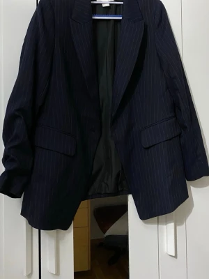 Mörkblå randig kavaj - Snygg mörkblå kavaj med tunna vita kritstrecksränder och klassisk passform. Kavajen har två fickor med lock framtill och är helfodrad. Perfekt för en stilren look och passar till många olika outfits. 