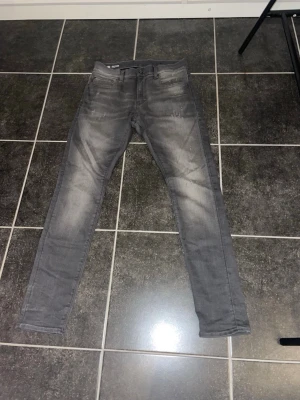 Grå slim fit jeans med slitningar - Snygga grå slim fit jeans med lätt slitna detaljer och klassisk femficksdesign. Jeansen har en smal passform och är tillverkade i stretchigt material för extra komfort. Perfekta för en trendig och avslappnad look.