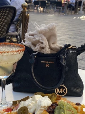 Svart Michael Kors handväska i läder - Snygg svart handväska från Michael Kors i strukturerat läder med guldfärgade detaljer och MK-hänge. Väskan har både handtag och justerbar axelrem, samt dragkedja upptill. Perfekt storlek för det viktigaste och en stilren look.