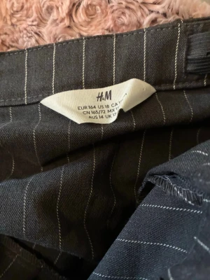 Grå kortkjol med vita ränder från H&M - Snygg grå kortkjol från H&M med vita tunna ränder och plisserad nederdel. Kjolen har en klassisk och trendig look som passar perfekt till många olika outfits. Perfekt för dig som gillar en stilren och modern vibe.