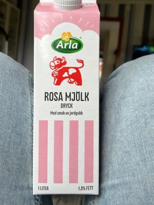 Arla rosa mjölkdryck jordgubb 1L - En 1-liters förpackning rosa mjölkdryck från Arla med smak av jordgubb. Kartongen är vit med rosa ränder och har en röd ko på framsidan. Innehåller 1,0% fett och är perfekt för dig som gillar smaksatt mjölk