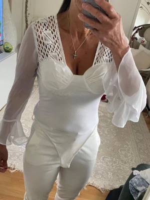 Vit body med spets och volangärmar - Snygg retorik vit body med transparenta volangärmar och spetsdetaljer över axlarna. Kupade bröst och figurnära passform. Har köpt den från usa år  1993. Storlek är fri storlek passar som s -?m den är stretch. Materialet är en mix av spets och tunn mesh.
