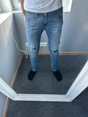 Replay anbass jeans med slitningar - Säljer ett par ljusblå skinny jeans med slitningar och hål på knäna. Jeansen har klassisk femficksdesign och dragkedjegylf. Perfekta för en avslappnad och trendig look.