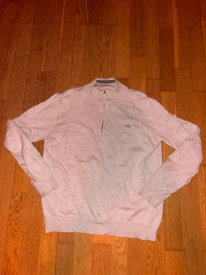 Beige halvzip-tröja från Gant - Beige långärmad tröja från Gant med halv dragkedja och liten broderad logga på bröstet. Tröjan har ribbade muddar vid ärmslut och nederkant samt en klassisk ståkrage. Perfekt för en stilren och avslappnad look. Passar en som är 165 cm lång ungefär. 
