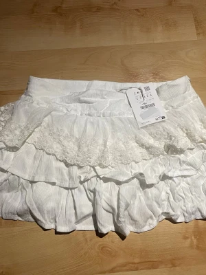 Vit mini volangkjol från Pull&Bear - Vit volangkjol från pull and bear. Helt ny. Kjolen har shorts under. Dragkedjan är lite trög något som var när jag köpte den, just denna modell på kjol verkar haft de problemet så inget fel på kjolen i sig.