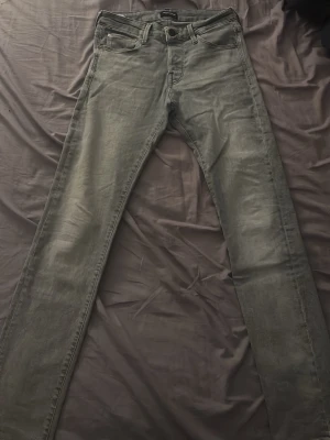 Grå slim fit jeans från jack&jones - Säljer ett par grå slim fit jeans från jack&jones Jeans med klassisk femficksdesign och snygga detaljer på bakfickorna. Jeansen har en något tvättad look och är tillverkade i bomull med stretch för extra komfort.