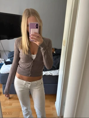 Stickad kofta - Säljer en brun/beige stickad kofta med rund halsringning och knäppning framtill. Koftan har långa ärmar och är tillverkad i ett mjukt, tunt material. Storlek Xs och den är helt ny och oanvänd med lapp från Hm