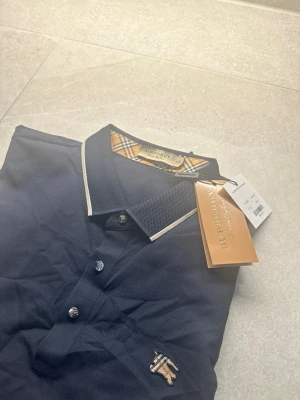 Burberry Polo Shirt - Tjenare, säljer faderns Burberry Polo Shirt. Riktigt fin och exklusive polo tröja med accenter av burberrys färger och mönster runt kragen och i hästen. Skick 10/10 nästan sprillans ny endast testad och följer med lappar, Storlek: XL men sitter som en L/M. Luftig och skön polo tröja inför sommaren 👏