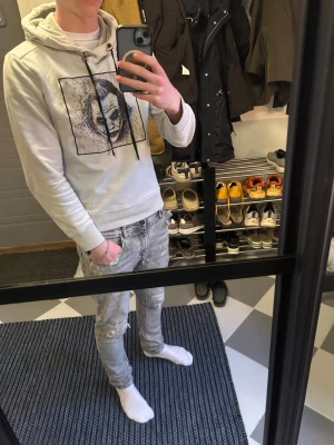 Limitato hoodie vit - Säljer en vit limitato hoodie med huva och snörning. På bröstet finns ett stort grafiskt tryck i svart med ett ansikte i konstnärlig stil. Hoodien har ribbade muddar vid ärmslut och nederkant. Perfekt för dig som gillar streetwear och vill sticka ut lite extra. Troligen i syorlek s då det inte står.