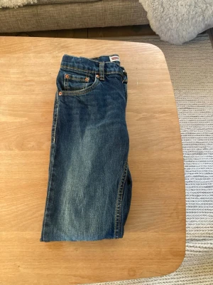 Levi's 501 blå jeans med raka ben storlek 12A - Klassiska blå Levi's 501 jeans med raka ben, femficksmodell och tydliga kontrastsömmar. Jeansen har den ikoniska läderpatchen bak i midjan och Levi's röda etikett på bakfickan. Tillverkade i slitstarkt bomullsjeansmaterial.