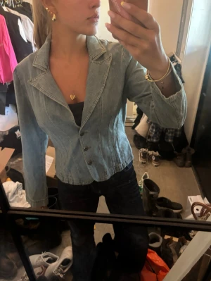Ljusblå figursydd jeansjacka - Snygg ljusblå jeansjacka med figursydd passform och klassisk krage. Jackan har långa ärmar och knäpps med fyra metallknappar framtill. Perfekt för dig som vill ha en trendig och stilren look.