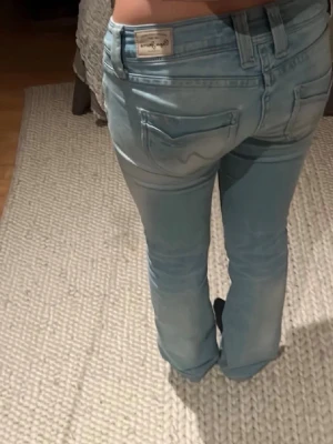 Ljusblå raka Pepe jeans från London. Lågmidjade och bootcut. - Säljer ett par ljusblå jeans med rak passform och klassisk femficksdesign. Jeansen har normal midja och är lågmidjade och bootcut och tvåknappig.