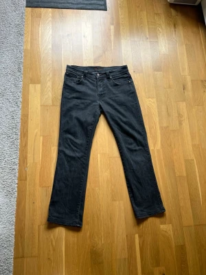 Nudie Jeans – Slim Jim, Dry Black Coated  - Säljer ett par snygga Nudie Jeans i modellen Slim Jim i färgen Dry Black Coated. Jeansen är i 98% bomull och 2% elastan, vilket ger en bekväm passform med lite stretch.  Skick: Använt men i gott skick. Naturlig blekning/fading som hör till stilen.  Storlek: W33 / L32 (sitter mer som 32/30 i praktiken)  Uppmätta mått (liggande): • Midjemått: ca 42 cm (x2 = 84 cm runt) • Ytterbenslängd: ca 95 cm • Benöppning: ca 20 cm