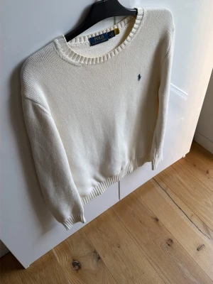 Vit stickad tröja från Polo Ralph Lauren - Klassisk vit stickad tröja från Polo Ralph Lauren med rund halsringning och diskret broderad logga på bröstet. Tröjan har ribbade muddar vid ärmslut och nederkant. Perfekt för en stilren och enkel look. 8/10 skick Mvh ItsForfits 🌟Krämvit!