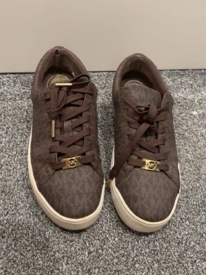 Bruna Michael Kors sneakers med monogram - Snygga bruna sneakers från Michael Kors med klassiskt MK-monogram över hela skon. Har använt de ett par gånger men inte mer än så 
