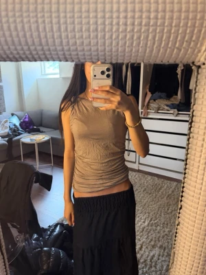 Beige ärmlös linnetopp - Snygg beige ärmlös linnetopp med tight passform och rynkade detaljer längs sidorna. Perfekt att styla med både kjol och jeans för en trendig look. Enkel och stilren design utan synliga loggor eller mönster.