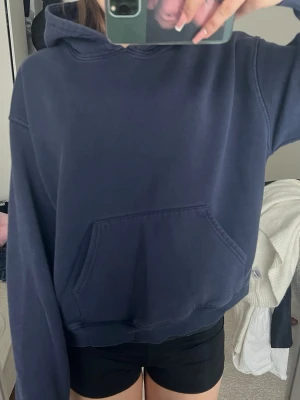 Mörkblå hoodie från Gina tricot  - En stilren mörkblå hoodie med huva och stor magficka framtill. Hoodien har en avslappnad passform och ribbade muddar vid ärmslut och nederkant. Perfekt för en chill och bekväm look. Materialet känns mjukt och skönt mot huden.