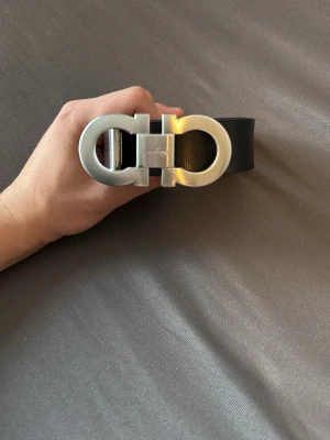 Ferragamo - Snyggt svart skärp från Salvatore Ferragamo med ett ikoniskt, stort silverfärgat dubbel-Gancini-spänne. Bältet är stilrent och passar perfekt till jeans eller kostymbyxor. Tillverkat i slätt skinn för en lyxig känsla.