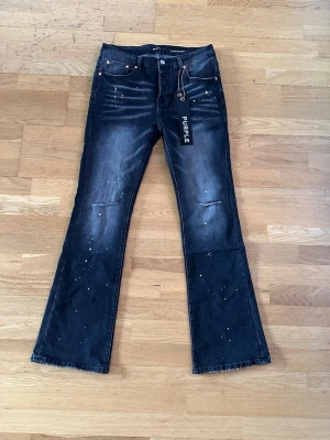Svarta flared jeans från Purple Brand - Snygga svarta flared jeans från Purple Brand med slitningar vid knäna och coola färgstänk. 