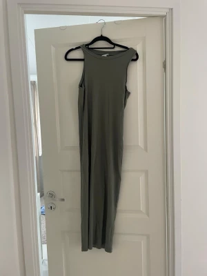 Grå ribbad långklänning - En stilren grå långklänning i ribbat material med ärmlös design och rund halsringning. Perfekt för en avslappnad och trendig look. Klänningen har en rak passform och är enkel att matcha med olika accessoarer.