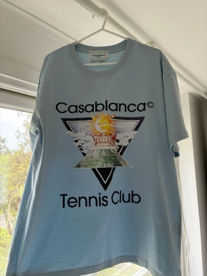 Casablanca t-shirt - Snygg ljusblå t-shirt från Casablanca med stort grafiskt tryck på bröstet och texten 'Tennis Club'. Klassisk rund hals och korta ärmar. Perfekt för dig som gillar streetwear och sportiga vibes.
