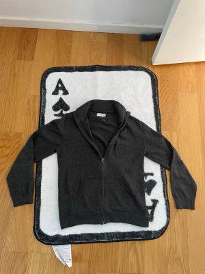 Mörkgrå zip-hoodie med fickor - Mörkgrå hoodie med dragkedja och två framfickor. Tröjan har ribbade muddar vid ärmslut och nederkant samt en klassisk huva. Perfekt för en avslappnad stil och enkel att matcha med andra plagg.