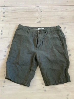 Gröna linneshorts från Dressmann - Helt nya! Köpte dem i höstas men fick aldrig chansen att använda dom för jag har växt sen dess och nu passar dem inte. Snygga gröna shorts från Dressmann i 100% linne. Klassisk modell med knapp och dragkedja framtill, bälteshällor och sidofickor. Perfekta för varma dagar när du vill ha en avslappnad men stilren look. Jävligt dåliga bilder! Orkar inte ta bättre. Kan skrivas ifall bra bilder krävs. Lite skrinkliga o så men det försvinner i tvätten eller om du ska strika dom eller hur du än gör. 