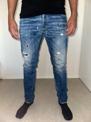 Blå slitna jeans med färgstänk - Säljer ett par blå jeans med skinny fit. Jeansen har klassisk femficksdesign och dragkedjegylf. Perfekta för en avslappnad streetstil. Används fåtal gånger