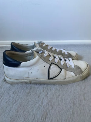 Vita Philippe Model sneakers - Snygga vita sneakers från Philippe Model med grå mockadetaljer och svarta partier vid hälen. Klassisk låg modell med vita skosnören och svart yttersula. Perfekta för dig som gillar stilrena och trendiga skor med exklusiv känsla. Använda fåtal gånger. Säljer eftersom de har blivit för små! Dm för frågor