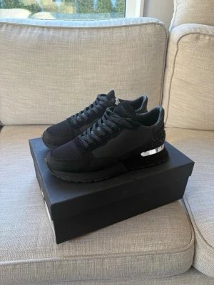 Svarta sneakers från Mallet London - Stilrena svarta sneakers från Mallet London med snygga detaljer i mesh och skinn. Skorna har snörning och en cool metallisk detalj på hälen. Perfekta för dig som gillar en clean och modern look.