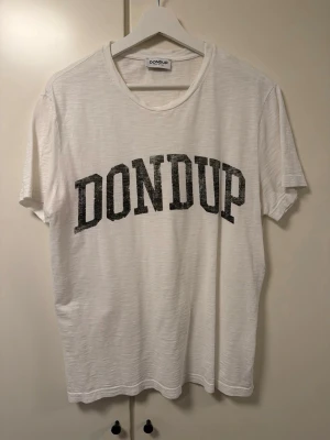 Vit t-shirt från Dondup - Vit t-shirt från Dondup med svart tryck över bröstet. Klassisk rund halsringning och korta ärmar. Tillverkad i mjuk bomull, perfekt för en avslappnad och stilren look.