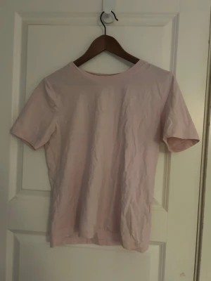 Ljusrosa t-shirt - En enkel och mjuk ljusrosa t-shirt från Gina Tricot, basically basics-kollektionen. Modellen är klassisk med rund hals och korta ärmar. Perfekt för dig som gillar stilrena och bekväma plagg. Materialet är bomull och passformen är normal. Säljer då den aldrig kommit till användning 