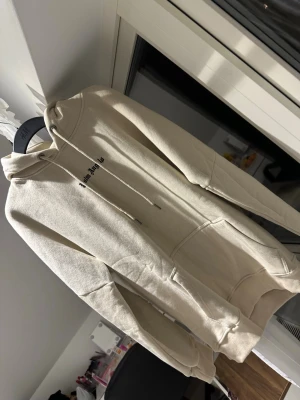 Beige hoodie med tryck - Snygg beige hoodie med liten svart text på bröstet. Klassisk modell med huva, dragsnören och stor magficka. Perfekt för en chill och avslappnad stil. Mjuk bomullsblandning som känns skön mot huden.
