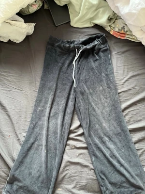 Mörkgrå mjukisbyxor från Donna - Mörkgrå mjukisbyxor från Donna med bred resår i midjan och vit dragsko. Byxorna har raka ben och är gjorda i ett mjukt, sammetsliknande material som känns riktigt skönt mot huden. Perfekta för chill dagar hemma eller när du vill vara extra bekväm.