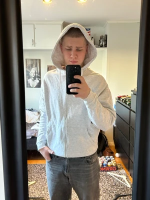 Ljusgrå zip-hoodie med huva - Säljer en ljusgrå hoodie med dragkedja och huva. Tröjan har två fickor framtill och ribbade muddar vid ärmslut och nederkant. Perfekt för chill dagar och enkel att matcha med jeans eller joggers. Materialet är mjukt och bekvämt, troligtvis bomullsblandning.