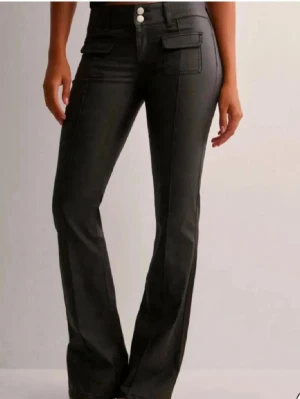 Svarta bootcut jeans med fickdetaljer - Snygga svarta bootcut jeans med två framfickor med lock och dubbla knappar i midjan. Skinnbyxor