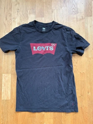 Svart Levi's t-shirt med logga - Svart t-shirt från Levi's med klassisk röd logga framtill. T-shirten har rund halsringning och korta ärmar. Tillverkad i mjuk bomull och har en normal passform. Perfekt för en avslappnad och stilren look.