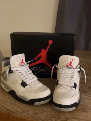  Jordan 4  - Säljer ett par Air Jordan 4 White Oreo sneakers med vit ovandel i läder, grå detaljer med svarta stänk, svarta och vita sulor samt röda Jumpman-loggor på plösen. Klassisk siluett med meshpaneler och plastdetaljer. Perfekta för dig som gillar streetwear och sneakerskultur.