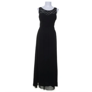 Svart långklänning med spetsdetalj - Elegant svart långklänning med spets upptill och rundad halsringning. Klänningen har breda axelband och ett flytande fall i kjolen. Perfekt för dig som vill ha en klassisk och stilren look med en touch av spets. Superfin till bal eller liknande! Köpt på sellpy men var tyvärr för stor, har även ordinarie lapp kvar. (Finns en liten ljus fläck mitt på klänningen som säkert går att få bort, skicka privat för bild)