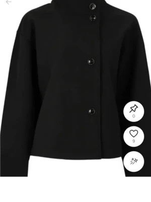 Svart ullkappa med bred krage - Stilren svart kappa i ull med bred, markerad krage och knäppning framtill. Modellen är boxig och har vida ärmar som ger en modern siluett. Perfekt för dig som gillar minimalistisk och trendig stil. nypris 500kr