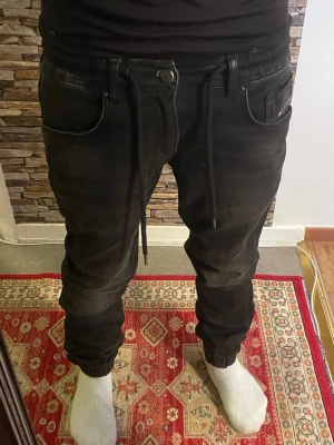 Svarta mjukisbyxor med dragsko - Svarta mjukisbyxor med avslappnad passform och resår vid bensluten. Byxorna har dragsko i midjan och flera fickor. Perfekta för en chill och bekväm stil. Materialet känns mjukt och stretchigt.