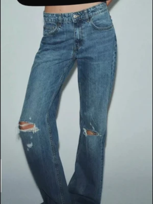 Blå slitna raka jeans - Snygga blå jeans med raka ben och slitningar på båda knäna. Jeansen har klassisk femficksmodell och hög midja. Perfekta för en avslappnad och trendig look.