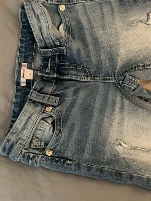 ljusblå jeans med slitningar - Säljer ett par blå lågmidjade jeans från Ginatricot med snyggt slitna detaljer och broderade bakfickor. Jeansen är från ginaypung i storlek 152. passar mig som är 156.