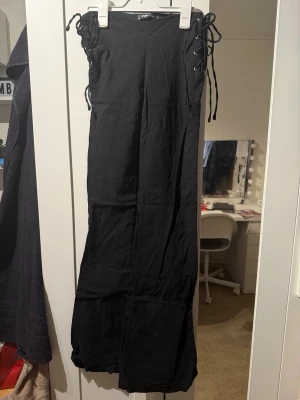 Svarta leggings med snörning i midjan - Säljer ett par svarta leggings med snörning i midjan på båda sidor. De har en rak passform och är tillverkade i ett stretchigt tyg som sitter bekvämt. Perfekta för dig som gillar en edgy och trendig stil.