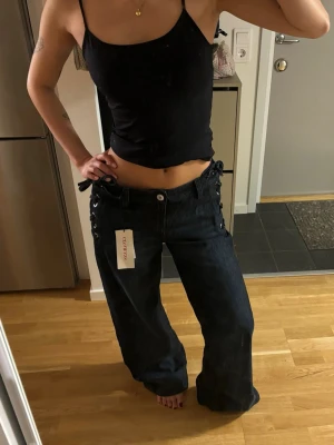 Ginatricot jeans - Säljer ett par svarta, vida jeans från ginatricot med cool snörningsdetalj i sidorna. Jeansen har hög midja, raka ben och klassiska fickor både fram och bak. Materialet är denim i bomull och de har en modern, avslappnad passform. Har storlek 34 också! Med prislapp! 💞