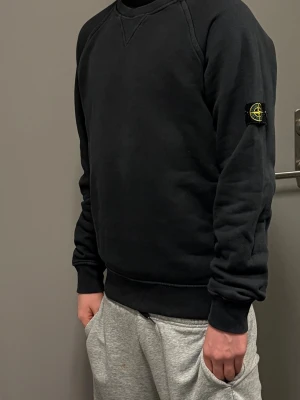 Svart sweatshirt från Stone Island -  (Personen på bilden är 172cm lång) Säljer en svart sweatshirt från Stone Island. Endast använd 3 gånger och är i mycket bra skick. Tröjan har den ikoniska Stone Island-loggan på vänster ärm och är tillverkad i mjukt bomullsmaterial. Perfekt för en avslappnad och stillig look.