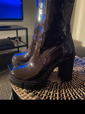 Vinröda stövletter från Aldo - Snygga Aldo vinröda stövletter i glansigt lackmaterial med kraftig blockklack och rundad tå. Dragkedja på insidan. Provat en gång. 